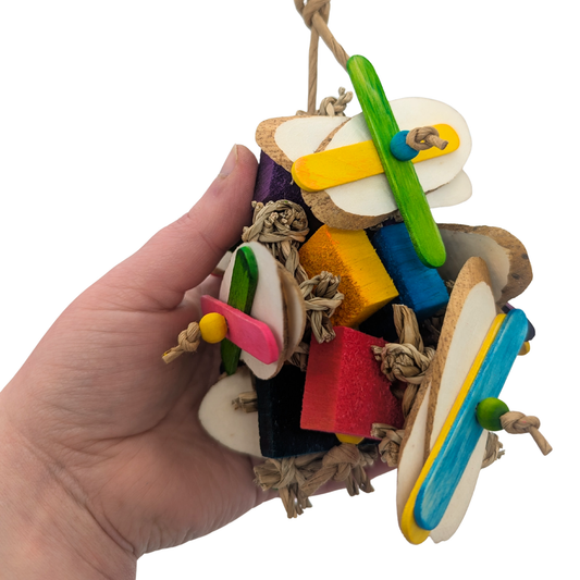 Flim Flam by Lil Monsters Bird Toys. A colorful bird toy made of seagrass, balsa wood, sola, and popsicle sticks. Held in hand for scale