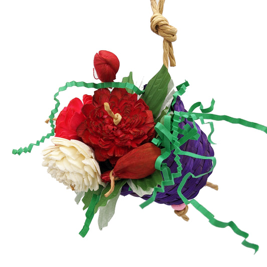 A bird toy with a basket, overflowing with 3 sola flowers dyed red, white, and pink. With shred paper and cupcake liners.