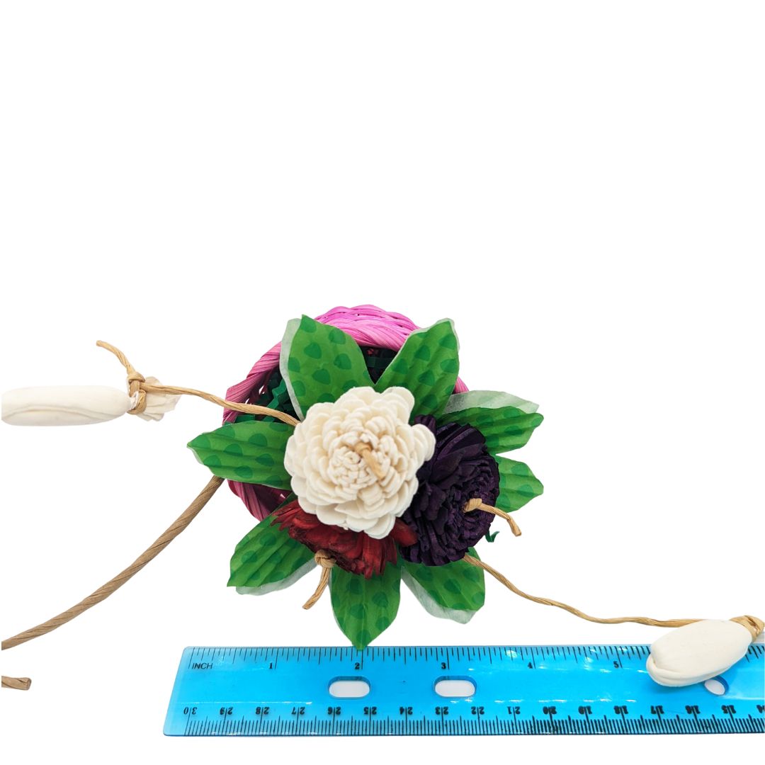 A bird toy with a basket, overflowing with 3 sola flowers dyed red, white, and pink. With shred paper and cupcake liners.