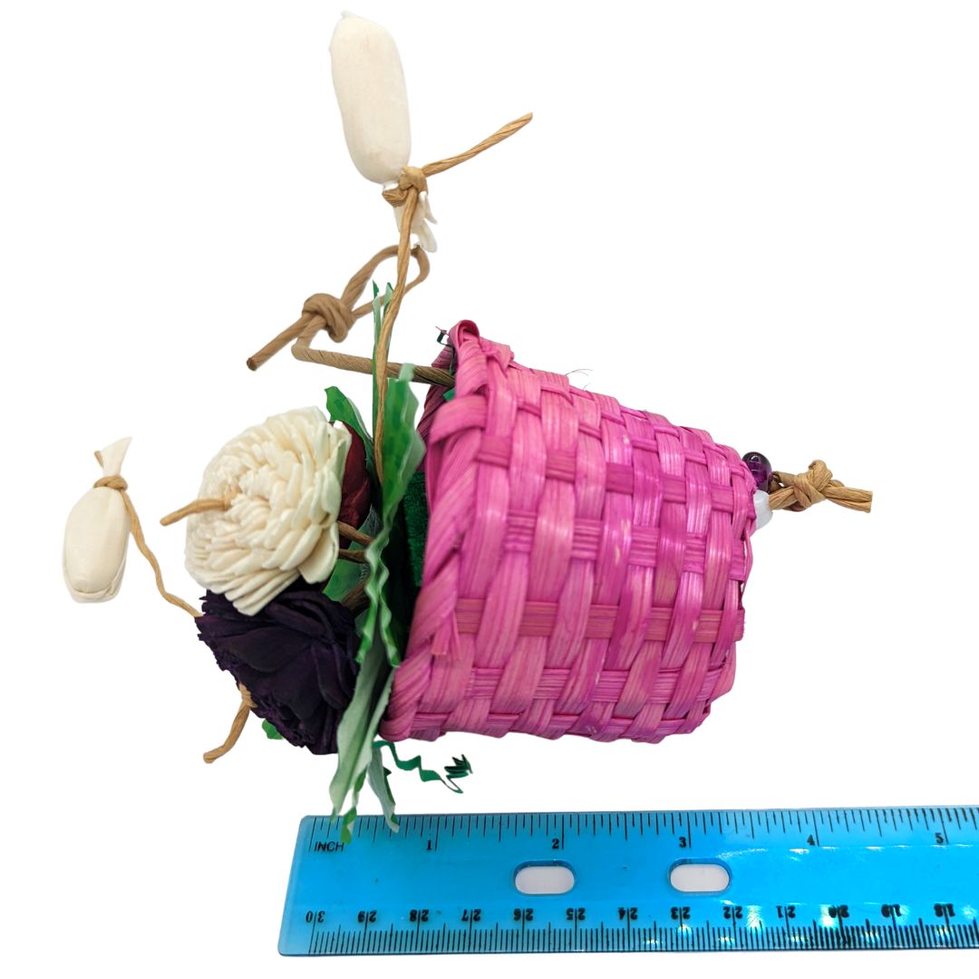 A bird toy with a basket, overflowing with 3 sola flowers dyed red, white, and pink. With shred paper and cupcake liners.
