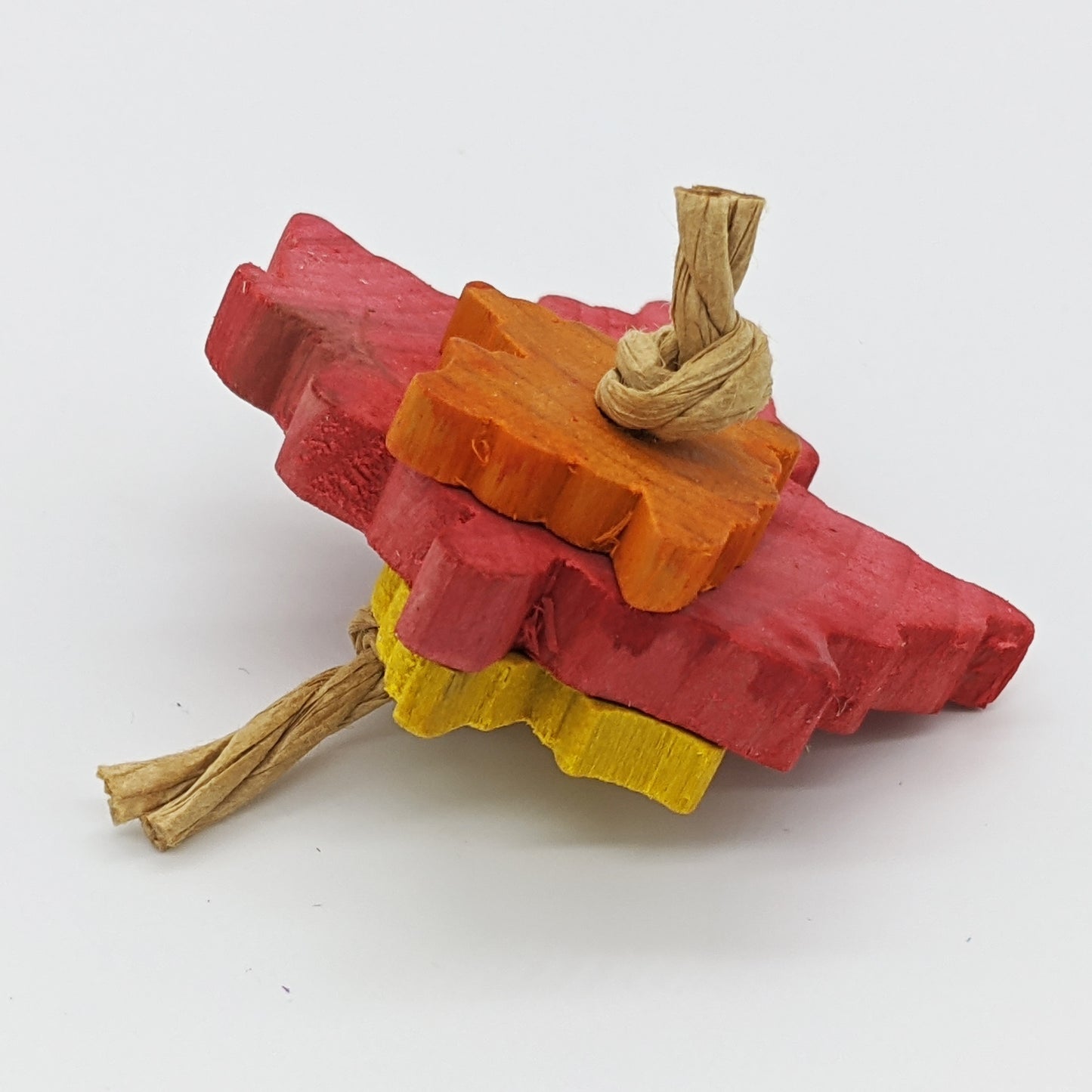 A natural hardwood bird toy. Picture shows a red large maple leaf with a smaller yellow and orange leaf tied on either side with paper rope. Leaves are about 1/4" thick.