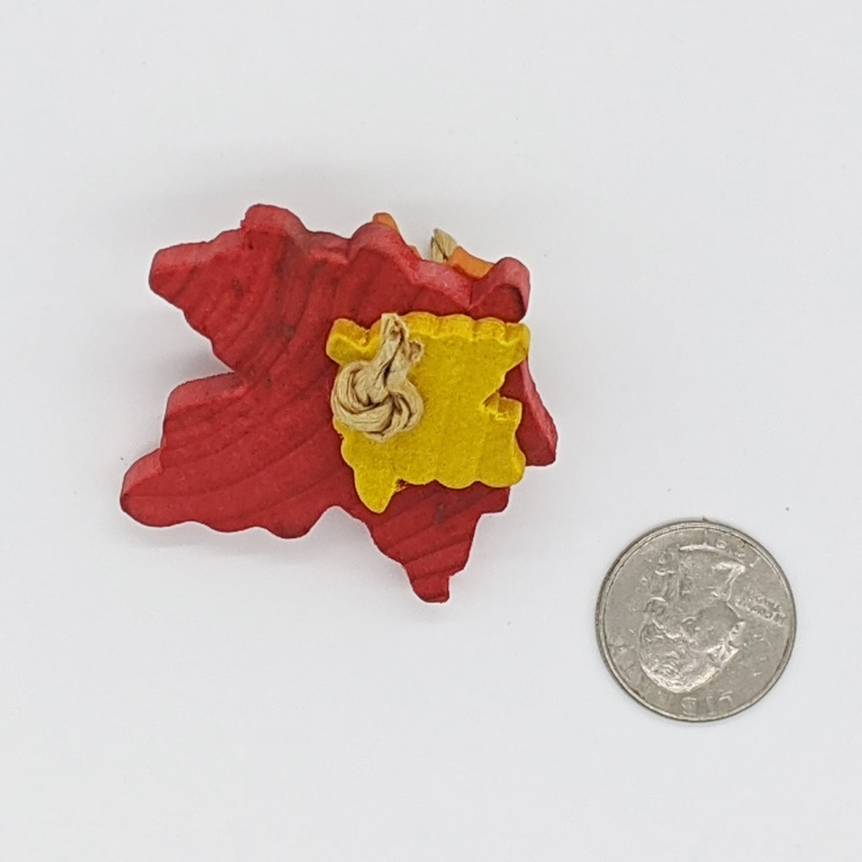 A natural hardwood bird toy. Picture shows a red large maple leaf with a smaller yellow and orange leaf tied on either side with paper rope. Leaves are about 1/4" thick. Shown with a US quarter for scale