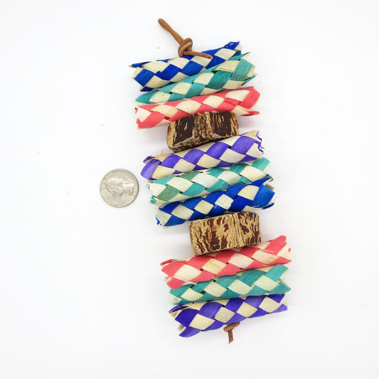 A colorful bird toy consisting of palm shredders and mahogany slices, strung together on a vertical paper rope.