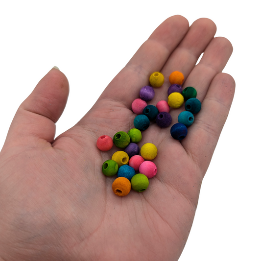 A set of 25 multicolored wood beads measuring 8mm, by Lil Monsters Bird Toys, held in hand for scale
