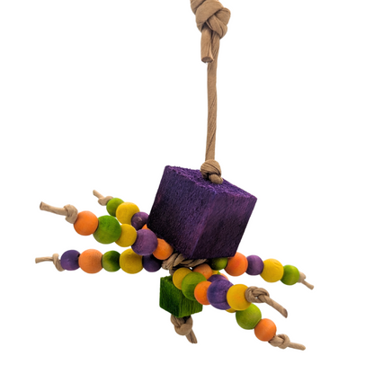 A halloween themed bird toy reminiscent of a spider. Beaded legs, square butt and head. Orange, green, purple, and yellow. Hanging from a paper rope on a white background.