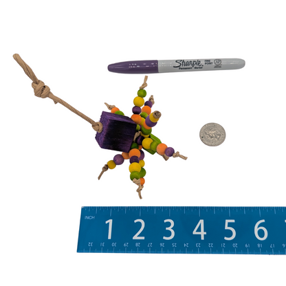 Colorful bird toy with beads and balsa block, next to a Sharpie marker, ruler, and coin for scale, on a white background.