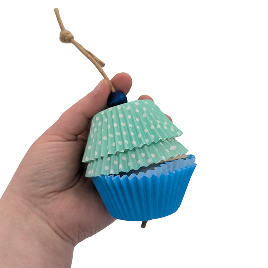 Cupcake Forager by Lil Monsters Bird Toys. A toy designed to resemble a cupcake with cupcake papers, a foraging cup, and a bead on top. Held in hand for scale. 