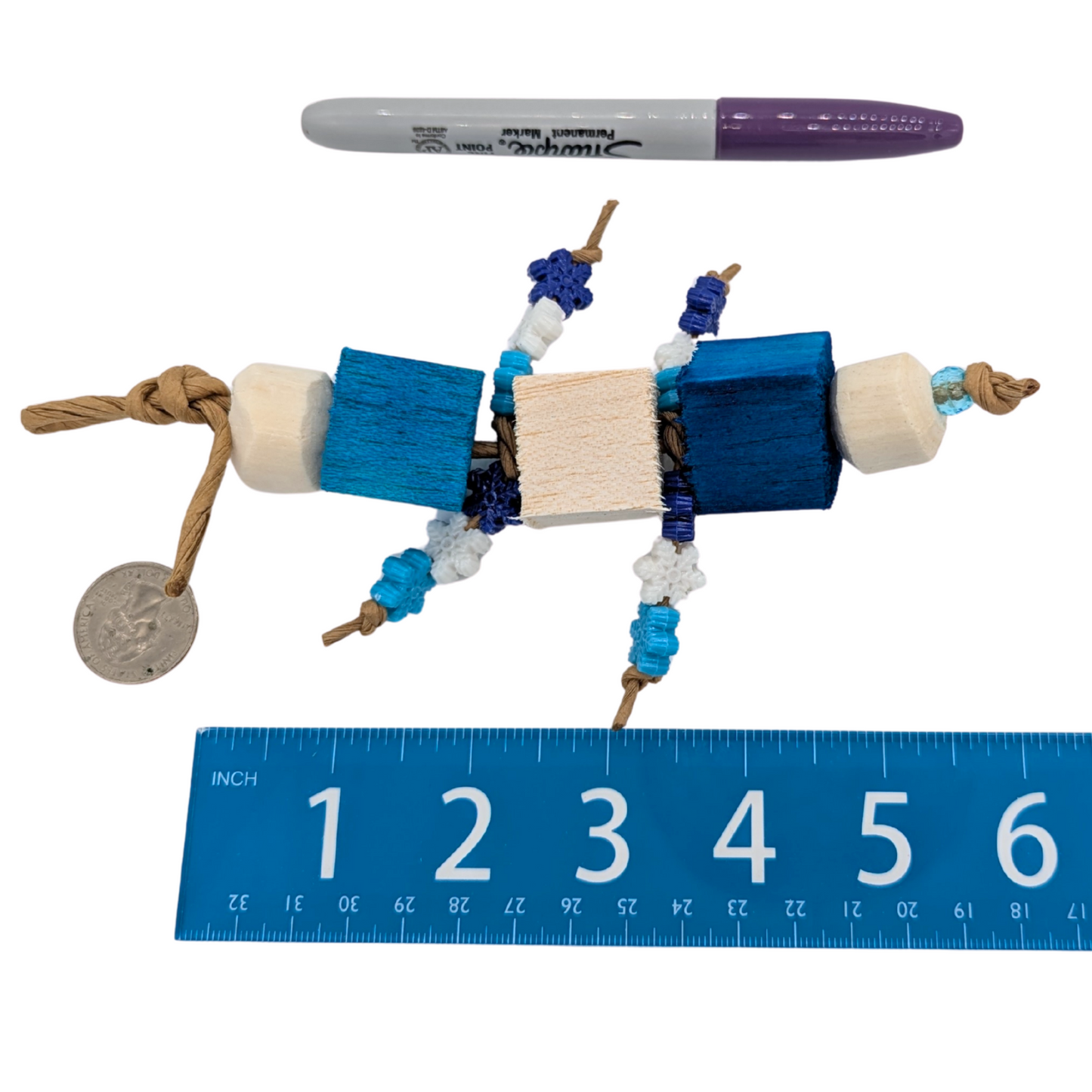 Bird toy with blue balsa blocks, sola rounds,, and plastic snowflake beads, set next to a sharpie marker, US quarter, and a ruler for scale