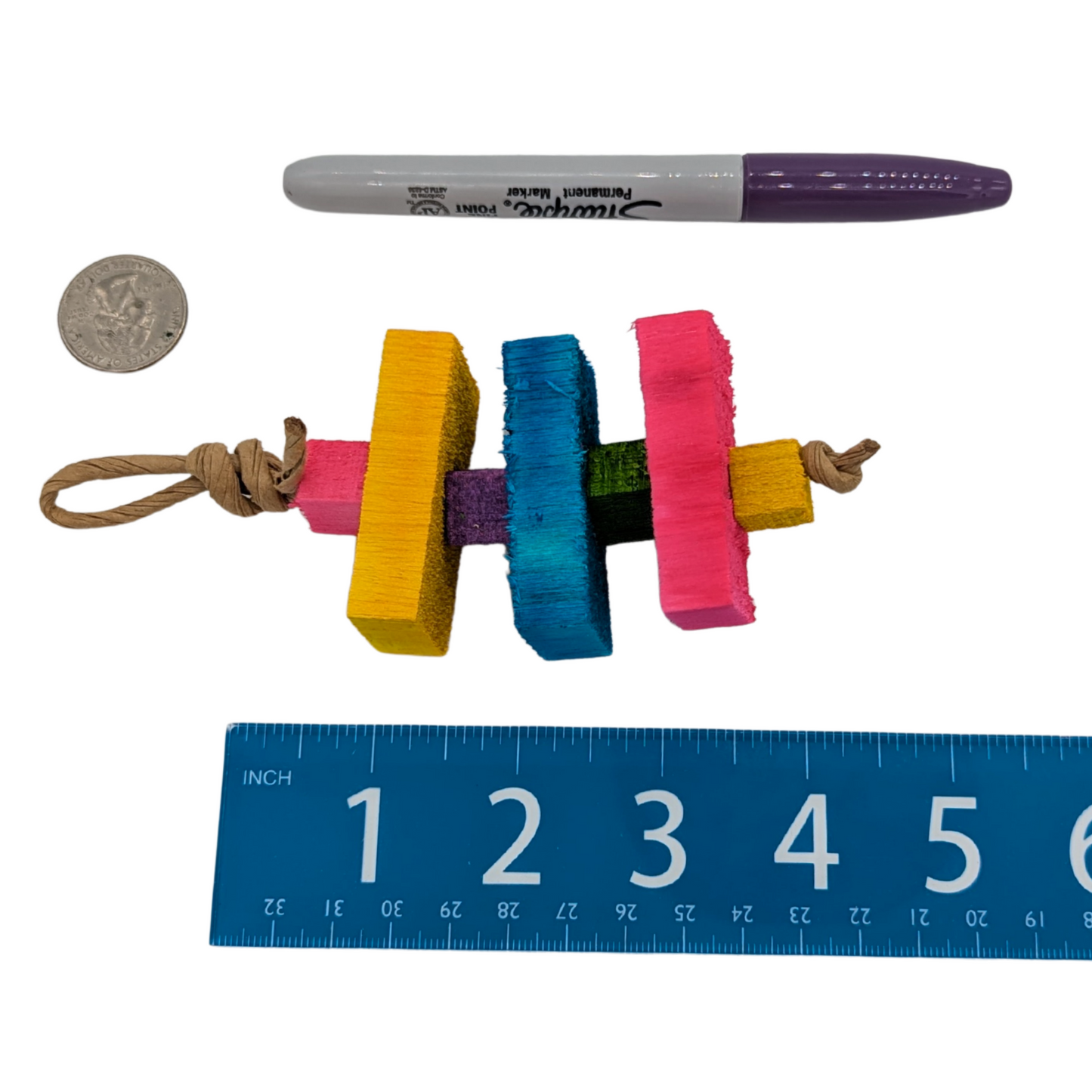 Colorful bird toy with a ruler, marker, and coin for scale on a white background