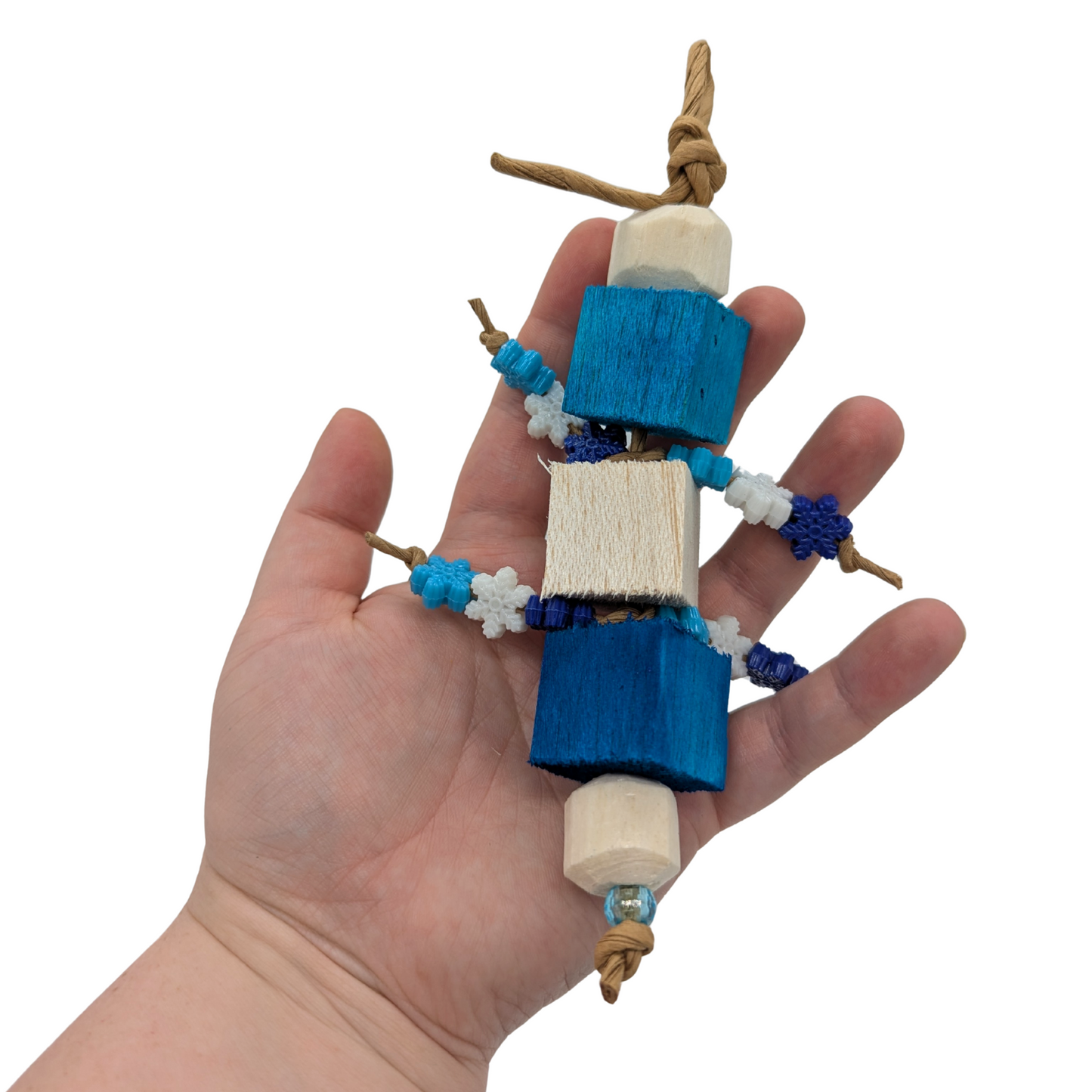 Hand holding a bird toy with blue balsa blocks, sola rounds,, and plastic snowflake beads on a white background