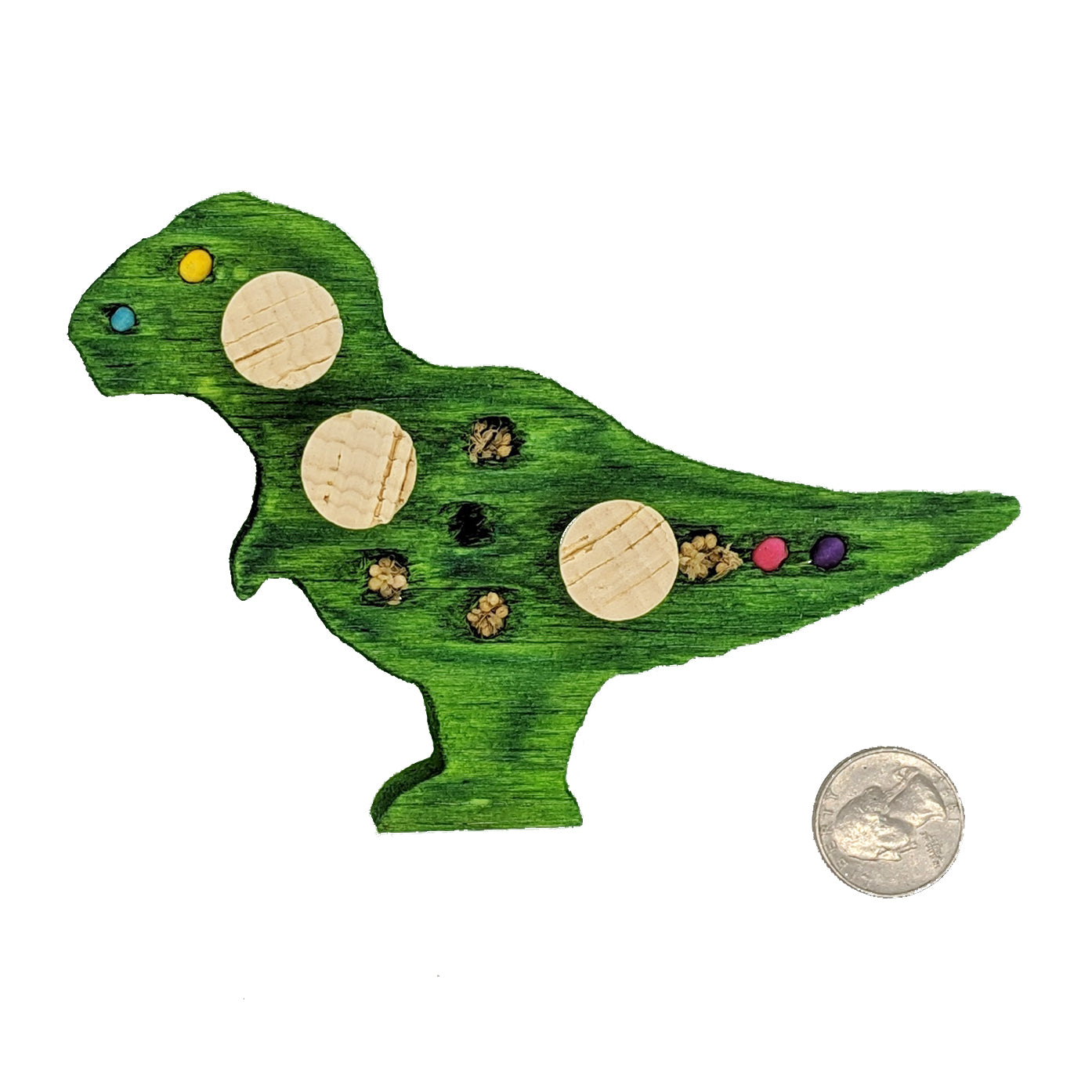 Balsasaurus Rex by Lil Monsters Bird Toys. A piece of balsa cut into the shape of a t-rex dinosaur. Embedded with cork stoppers, beads, and millet. Shown in a green color, next to a US quarter for scale. 