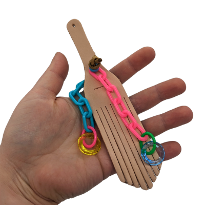 A hand holding a bird toy with a leather base and plastic additions on a white background. 
