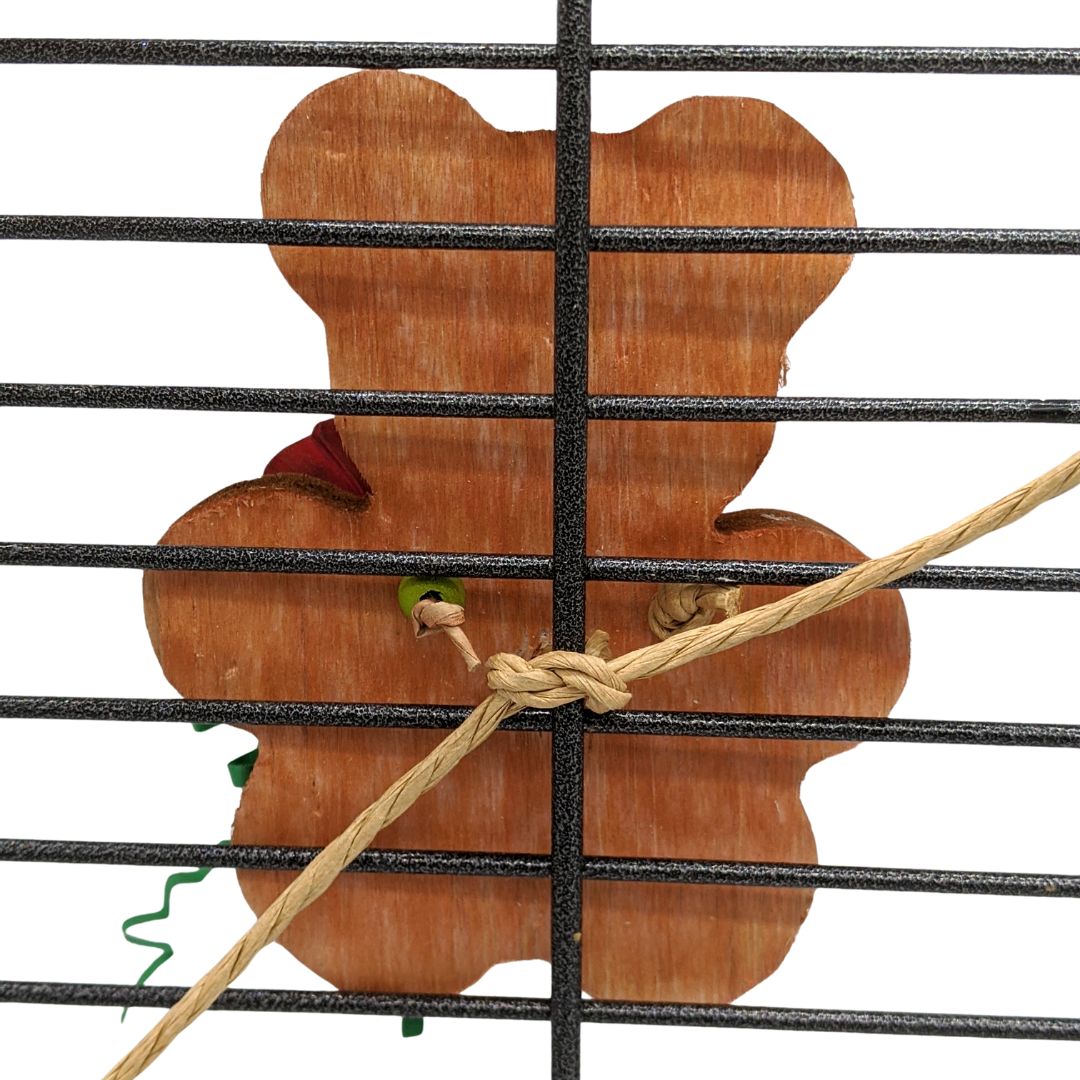 A teddy bear shaped piece of wood on cage bars, showing an example of the paper rope mounting option in use. 