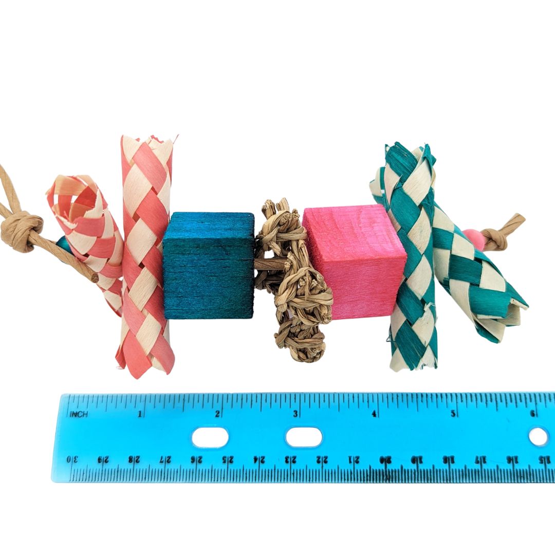 Bird toy with palm finger traps cut in half, two balsa blocks, and a piece of seagrass in the center. Shown next to a ruler for scale