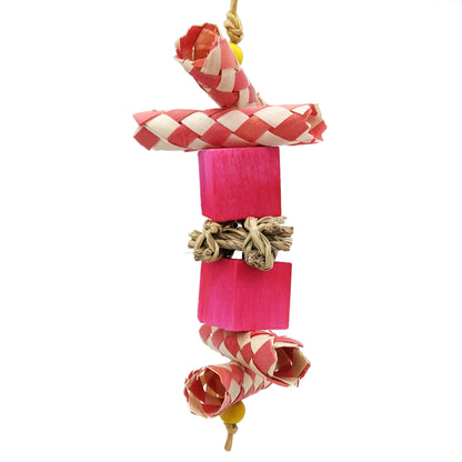 Bird toy with palm finger traps cut in half, two balsa blocks, and a piece of seagrass in the center. Pink coloration. 