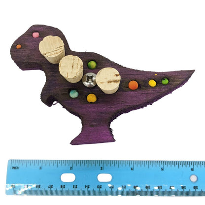 A tyrannosaurus rex shaped piece of balsa, with 4 small beads, 4 spots for millet or beads, and 3 cork stoppers. Shown with ruler at 6 inch wide