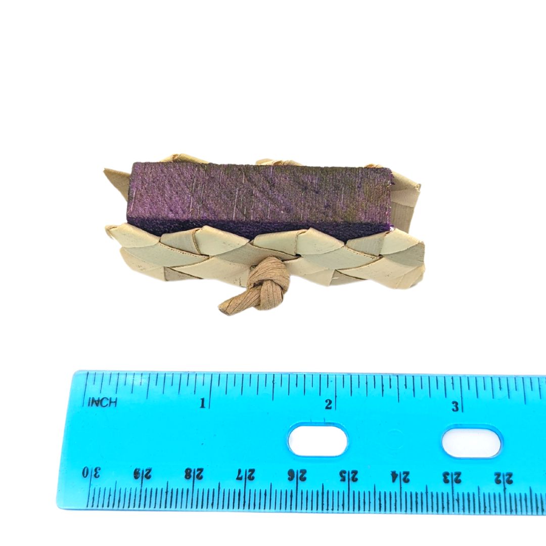 A foot toy for birds; piece of balsa in between two pieces of woven palm, held together with paper rope. Next to ruler showing 3 inch length 