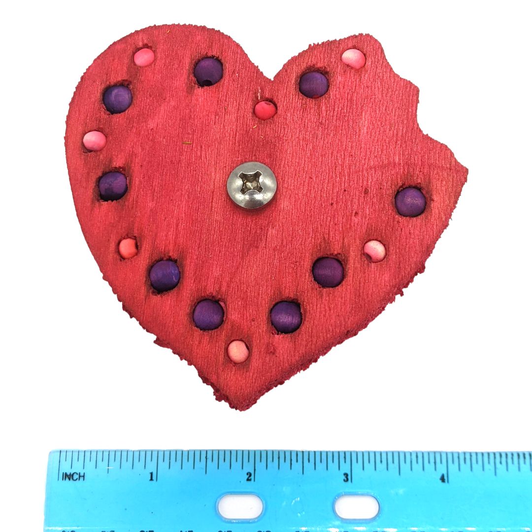 A heart shaped piece of balsa with a "bite" taken out of the right lobe. Embedded with 8mm and 6mm beads around the border.  Shown next to ruler, 4" wide