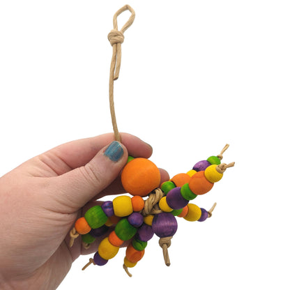 A hand holding a colorful beaded spider-inspired parrot toy made with wooden beads in various sizes and strung on paper rope.