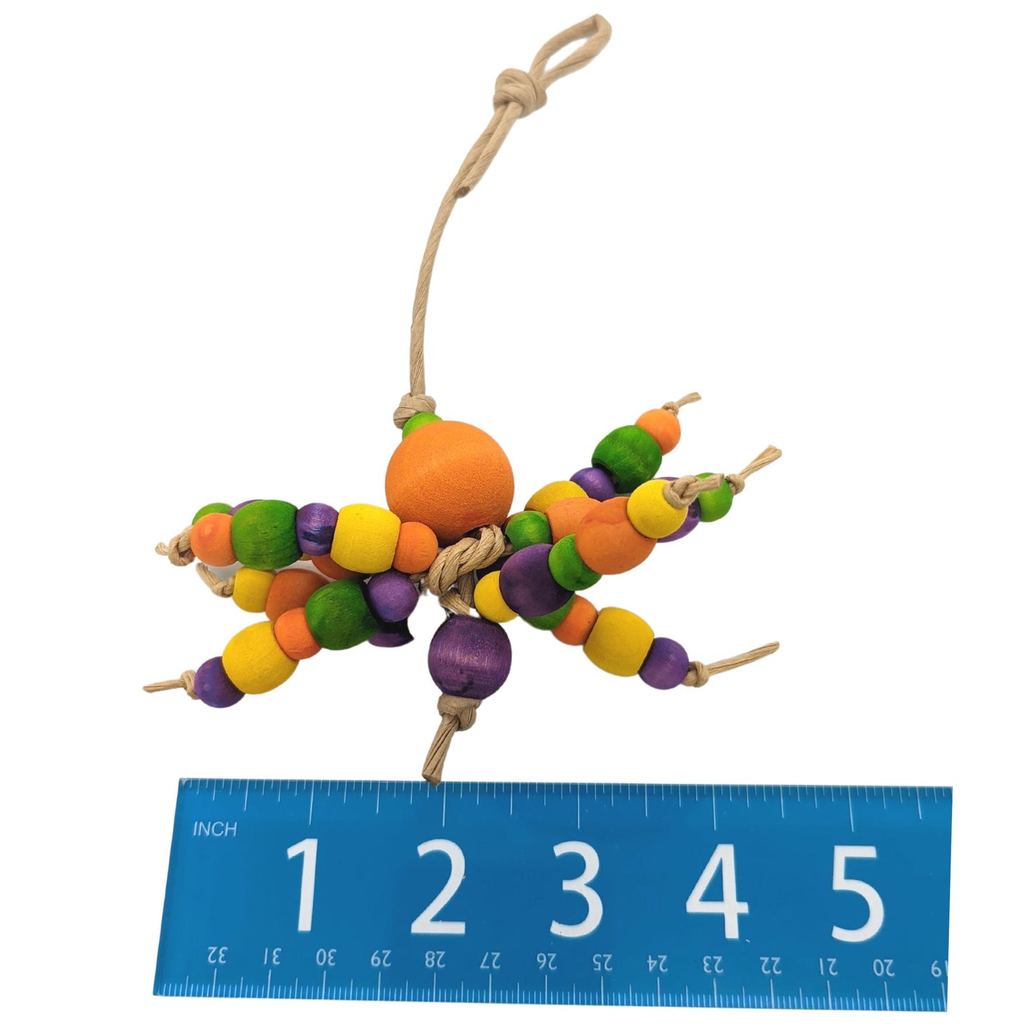 A colorful beaded spider-inspired parrot toy made with wooden beads in various sizes and strung on paper rope. Shown on a white background next to a ruler for scale. 