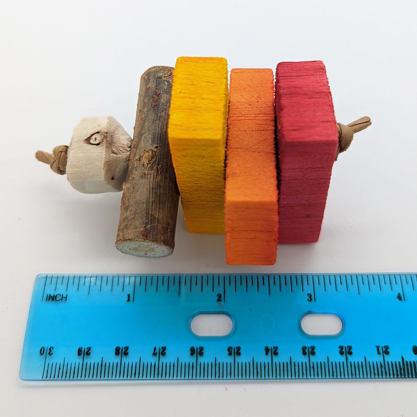 A summer foot toy with yellow, orange, and red balsa, and cottonwood stick, and sola bead. For small to medium birds as either a foot toy, small hanging toy, disabled birds, baby birds, or in a parrot carrier. Shown with a ruler, measures about 3 inches long. 