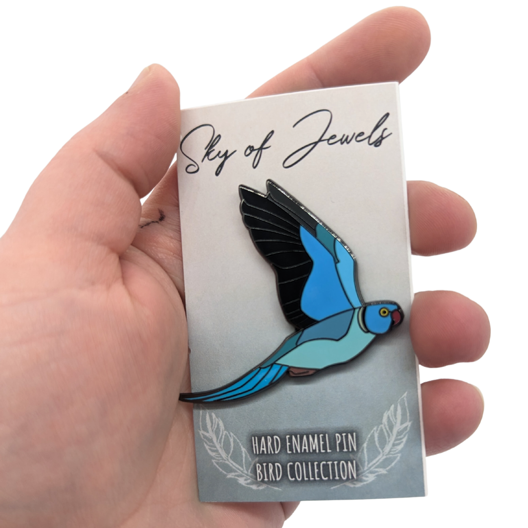 Blue Indian Ringneck Hard Enamel Pin by Roamin Bison Workshop, on card and in hand for scale. Card mentions Sky of Jewels, Hard Enamel Pin Bird Collection
