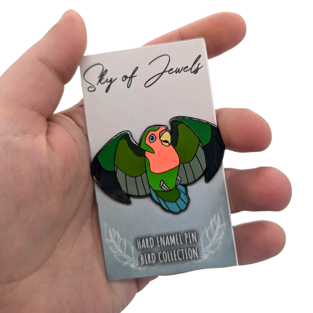 Lovebird Enamel Pin by Roamin Bison Workshop, on card and in hand for scale. Card mentions Sky of Jewels, Hard Enamel Pin Bird Collection